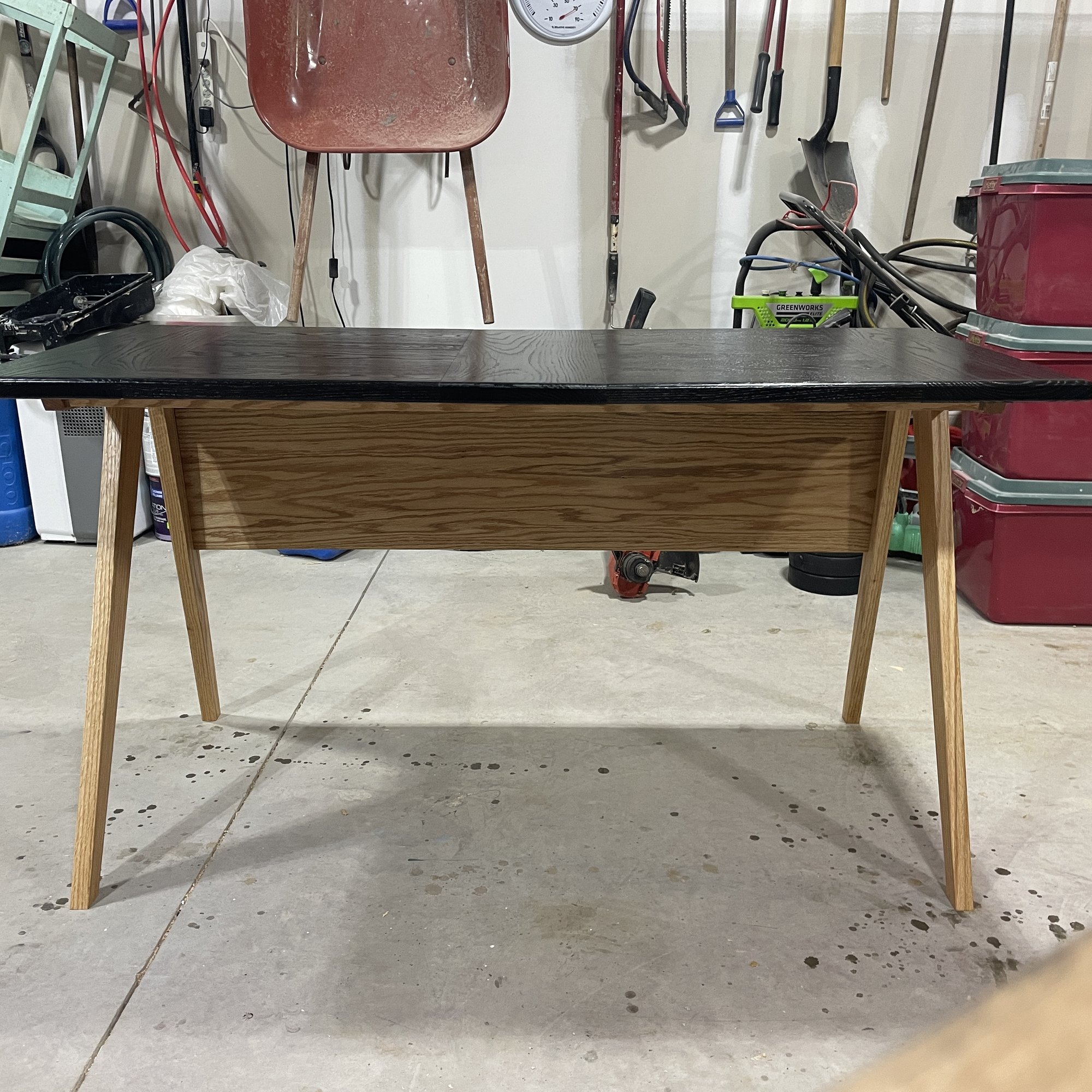Front view of the desk: ebonized oak top, natural oak apron, and four splayed legs.