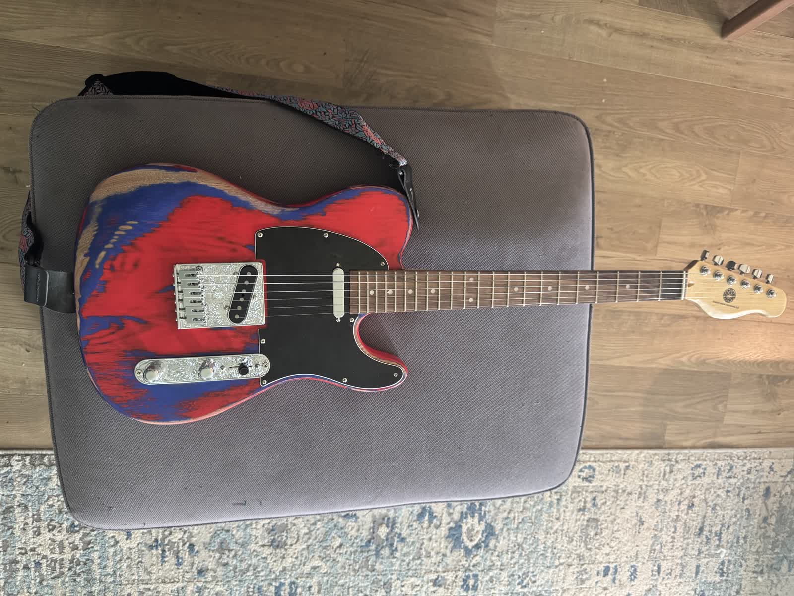 The completed Izzy custom T-style guitar with red and blue paint, black pickguard, engraved hardware, and Green Man Customs logo on the headstock.