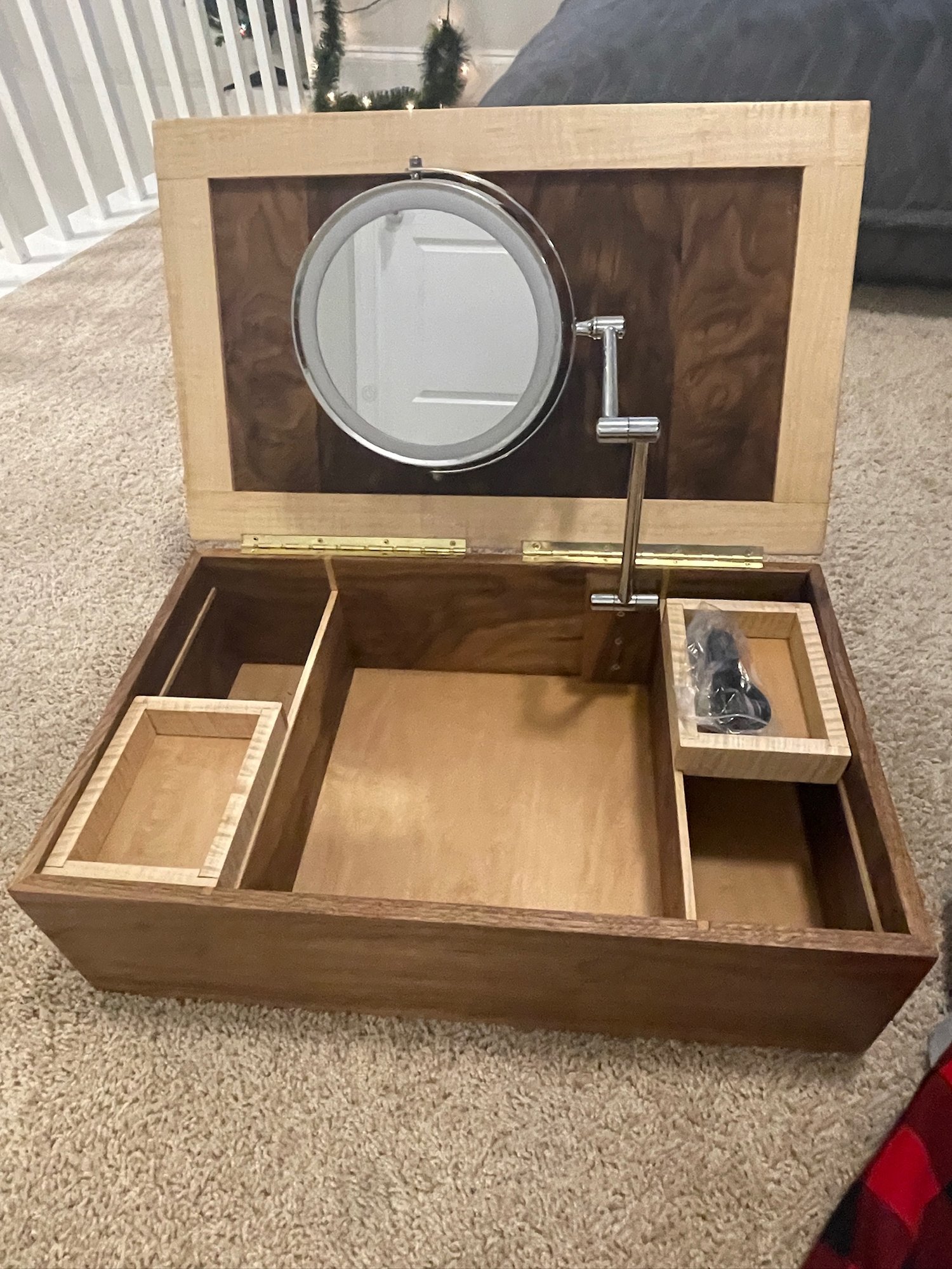 Open box with the lighted mirror raised on its arm, trays and a charging cable in the compartments.