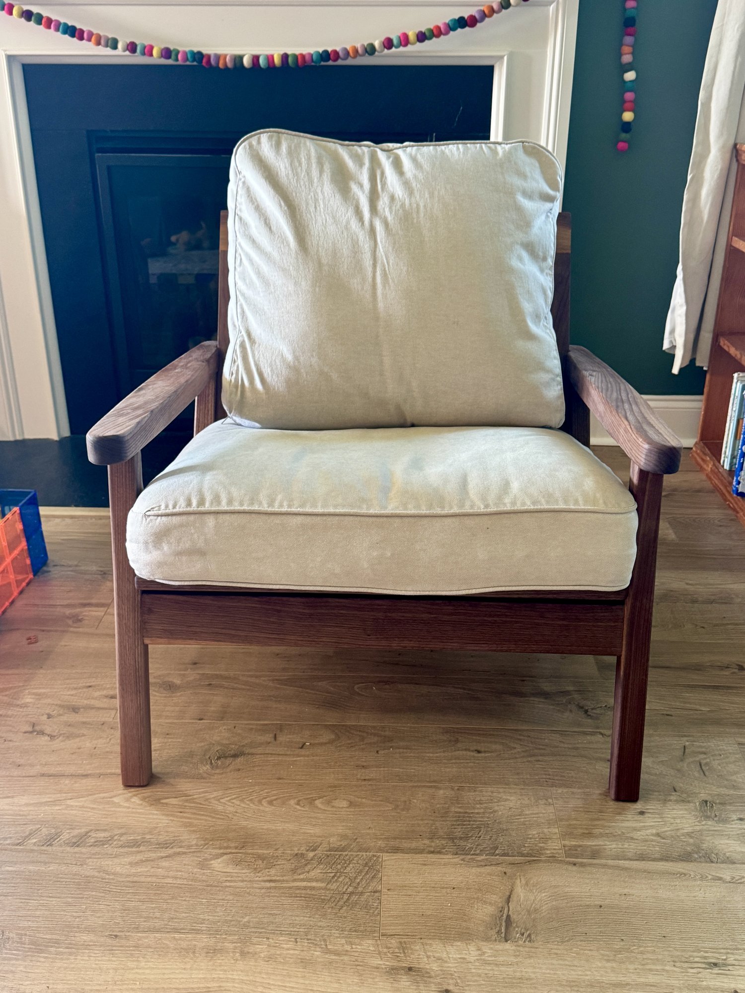 Front view of the mid-century walnut lounge chair with cream piped cushions and wide arms.