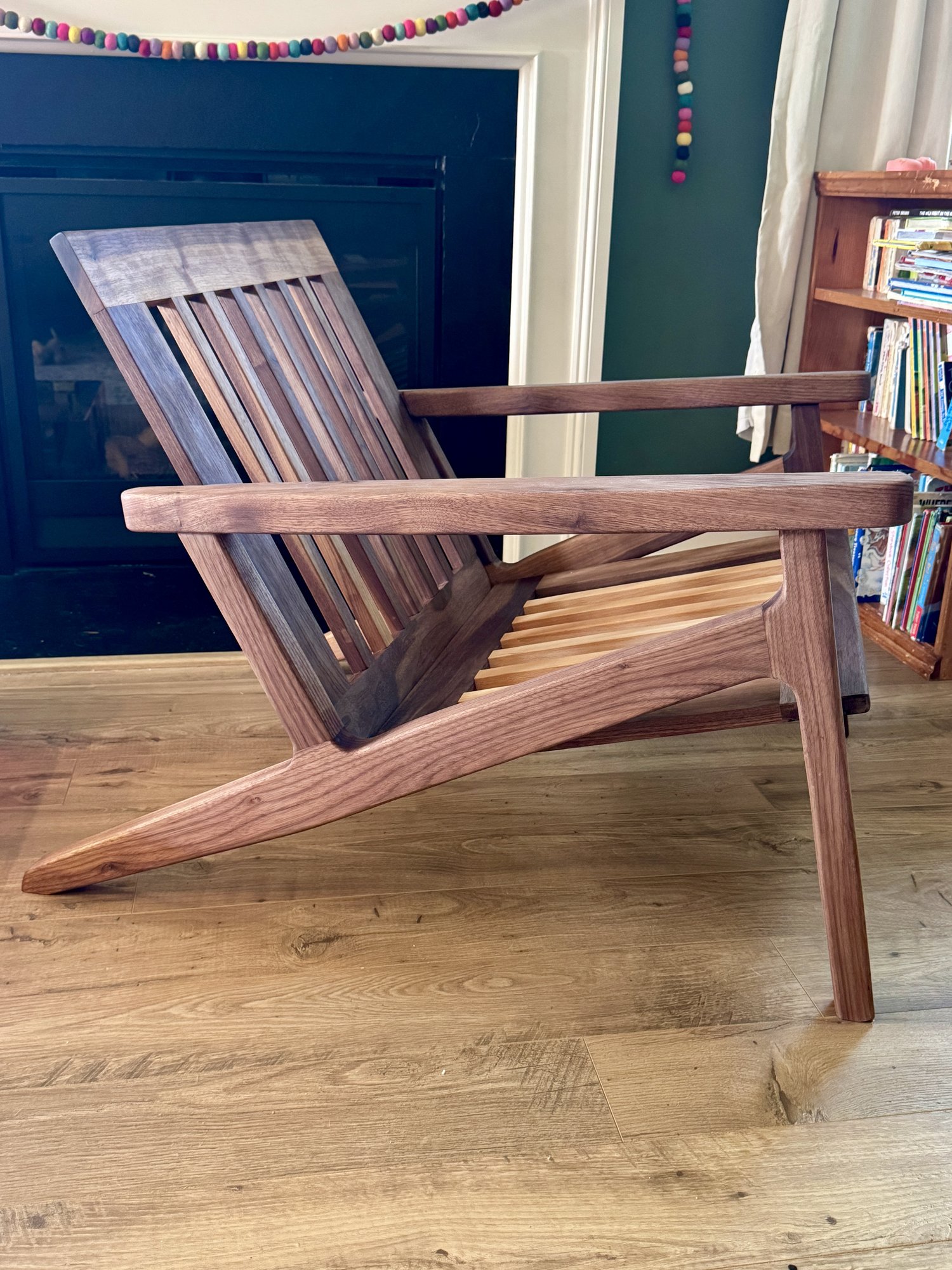 Side view of the walnut lounge-chair frame without cushions, showing the angled back, wide arm, and low recline.