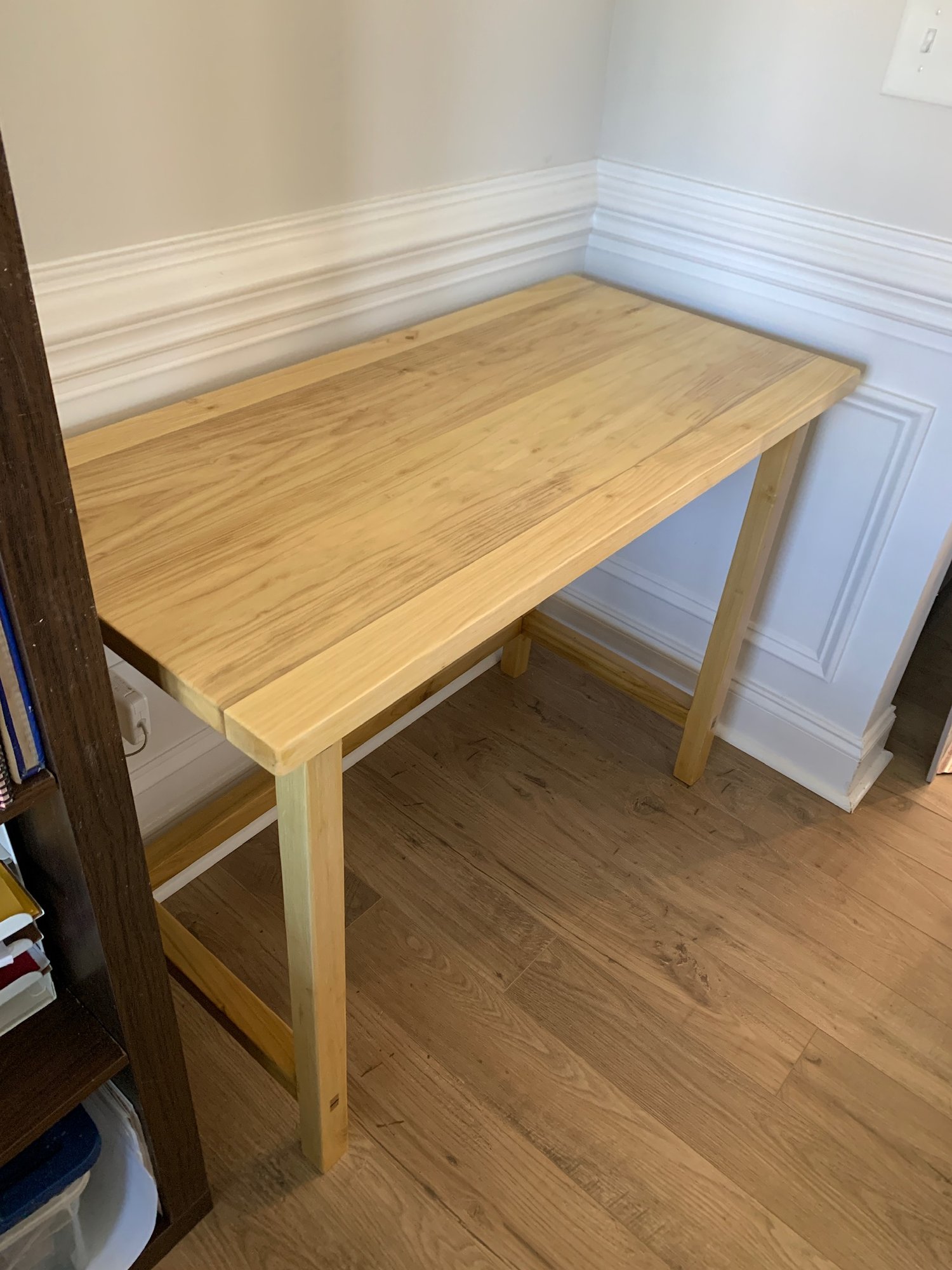 Corner view of the poplar desk showing the top, legs, and stretchers against a white wall.