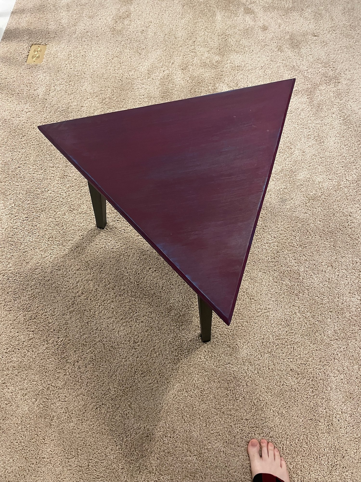 Top-down view of the triangular plum milk-paint top on three black legs.