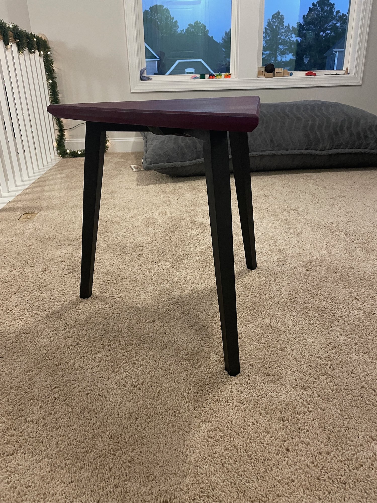 Low view of the table showing the black cabinet-paint legs and the thin plum top.