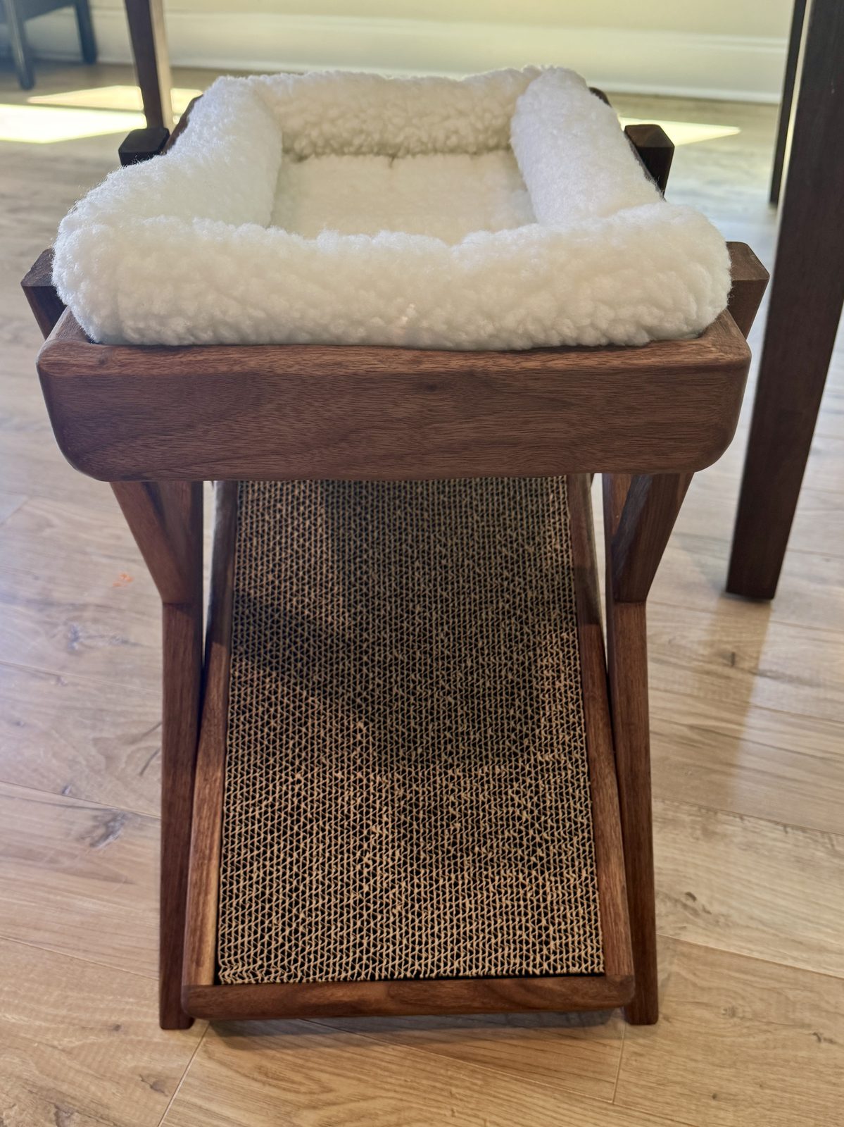 Closer three-quarter view of the cream sherpa bolster bed set in the walnut frame, with the cardboard scratch ramp below.