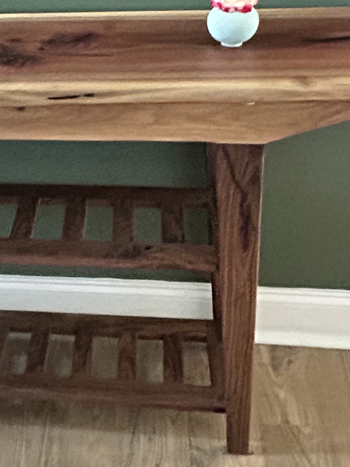 Close view of the walnut console’s live-edge top, right leg, and slatted shoe shelves.