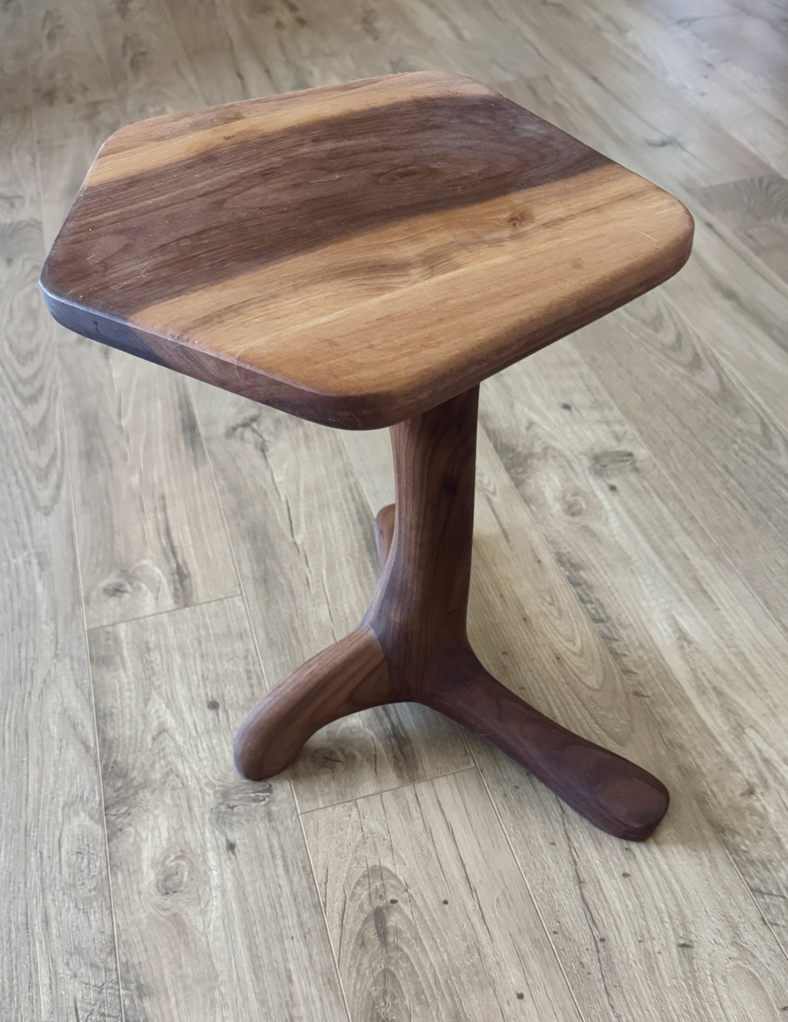 Angled view of the small walnut end table showing the organic top, turned stem, and three root-like feet.