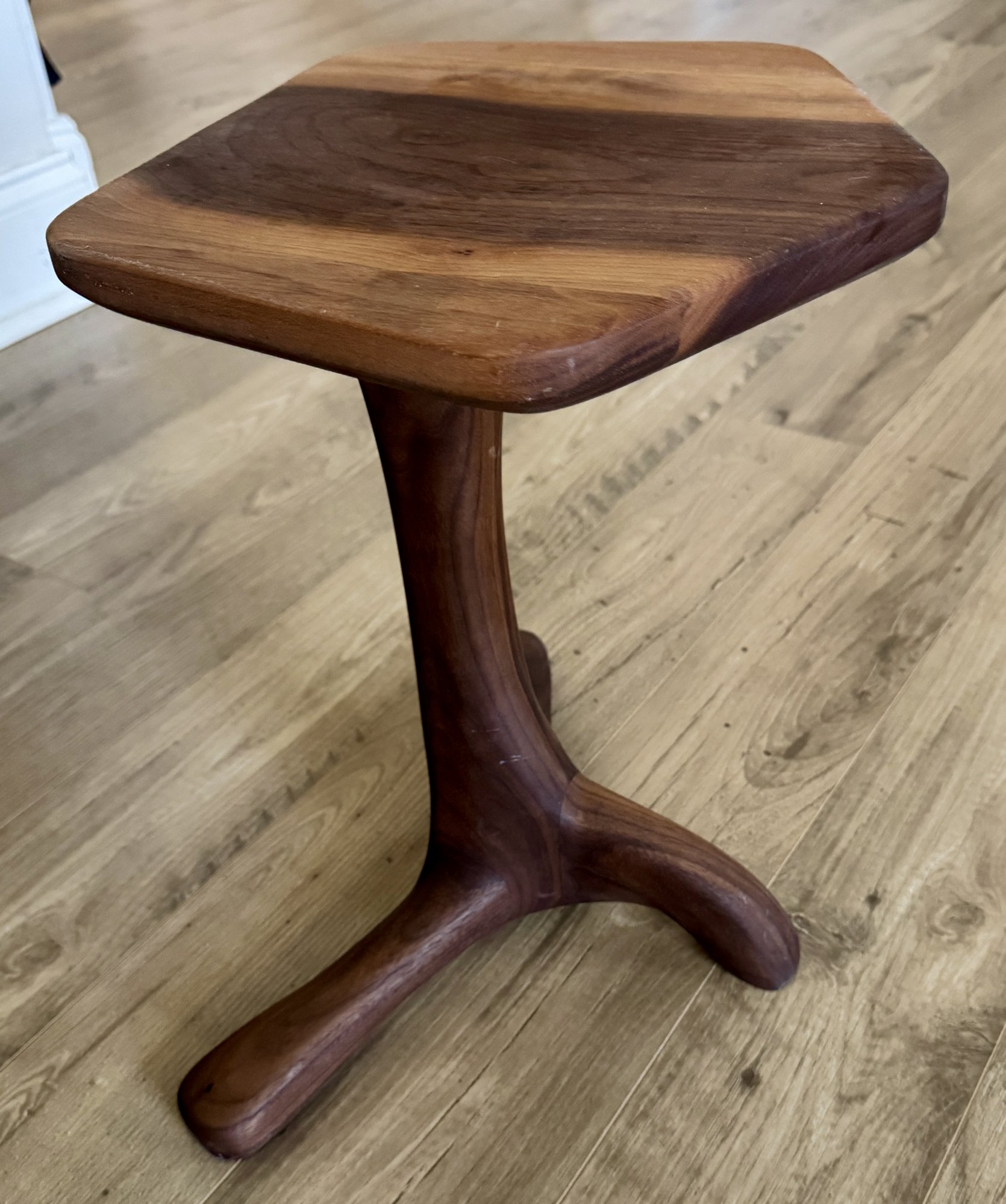 Three-quarter view of the walnut end table from above, showing the coffee-cup-scale top and tripod base.