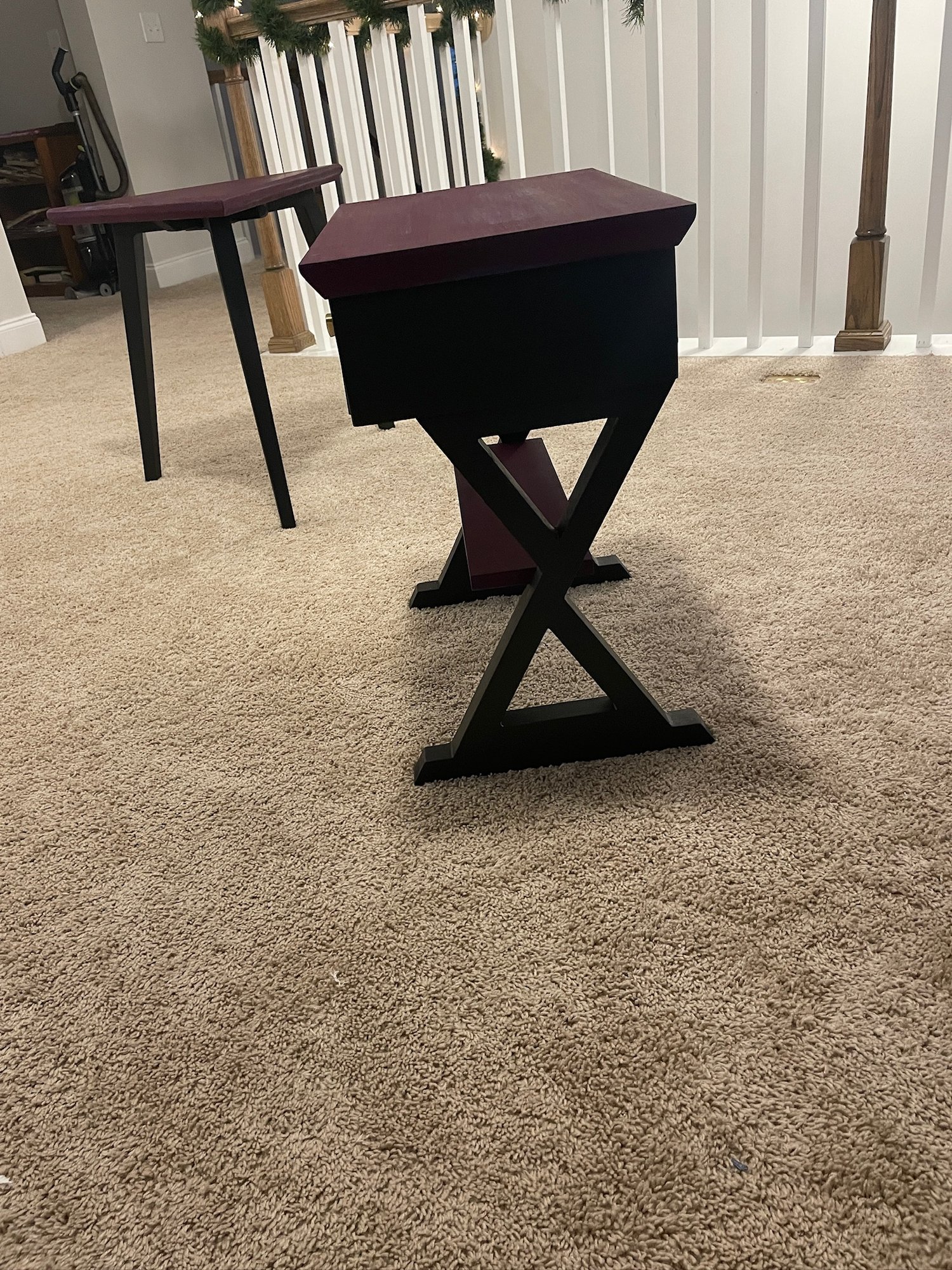 Side view of the X-frame end table beside the triangle reading table — same plum and black, different geometry.
